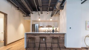 Et moderne køkken med en central ø, barstole og synlige ventilationsrør i loftet.