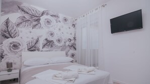 Ett sovrum med en blommig tapet, en säng med vita sängkläder, ett sängbord med en lampa och en tv som är monterad på väggen.