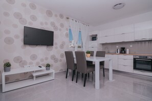Une cuisine moderne avec des armoires blanches, un four encastré et un coin repas comprenant une table et des chaises blanches.