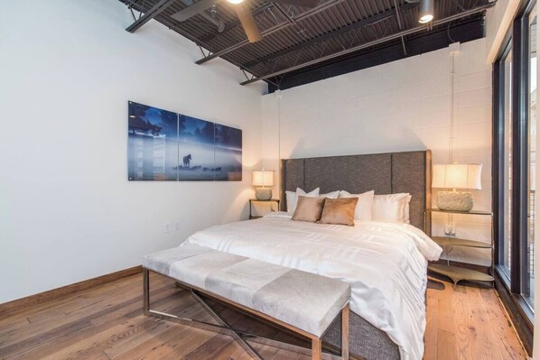 A modern bedroom with a large bed, wooden flooring, a mounted artwork, and bedside lamps. - This serviced apartment is a 2 bedroom(s), 2 bathrooms, located in Lexington, KY. (Lexington)