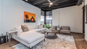 A modern living room with a white sectional sofa, a round coffee table, and a grey armchair. There is a painting on the wall and a plant on the coffee table. - This serviced apartment is a 1 bedroom(s), 1 bathrooms, located in Lexington, KY. (Lexington)