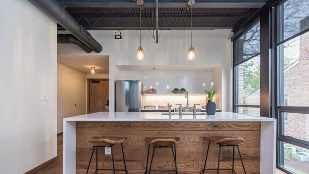A modern kitchen with a large island, bar stools, pendant lights, and a view through large windows. - This serviced apartment is a 1 bedroom(s), 1 bathrooms, located in Lexington, KY. (Lexington)