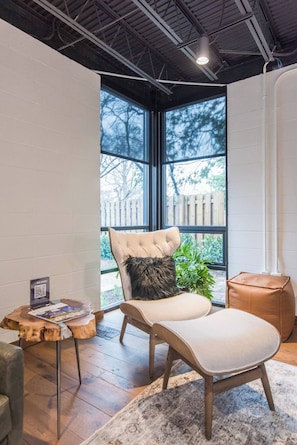 Ein moderner Lounge-Bereich mit gepolstertem Sessel, kleinem Holztisch und großem Fenster mit Blick ins Freie.