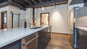 Eine moderne Küche mit einem Edelstahl-Kühlschrank, einer großen Kochinsel mit Spüle und einer Pendelleuchte.