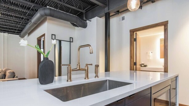 Eine moderne Küche mit weißer Arbeitsplatte, einem goldenen Wasserhahn und einer schwarzen Vase mit einer weißen Blume.