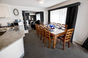 A modern kitchen with a dining area, featuring a wooden table and chairs, a built-in oven, and a clock on the wall. - Lakehouse on Waverley: Looking for a peaceful, relaxing getaway? (Paynesville)