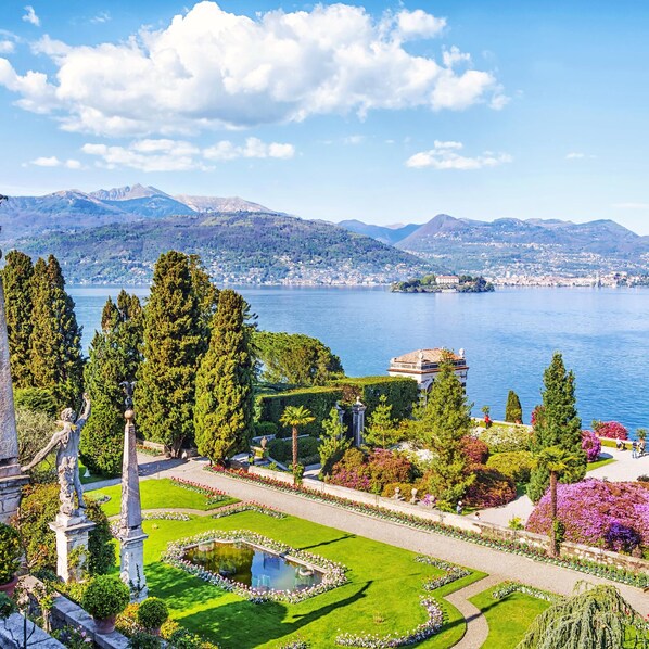 A landscaped garden with a central fountain, manicured lawns, and a view of a lake and distant mountains. - Residenza Oleandro Lake View Luino Center (Luino)