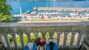 Un balcone con un tavolo apparecchiato per due, vista su una marina con barche e montagne sullo sfondo.