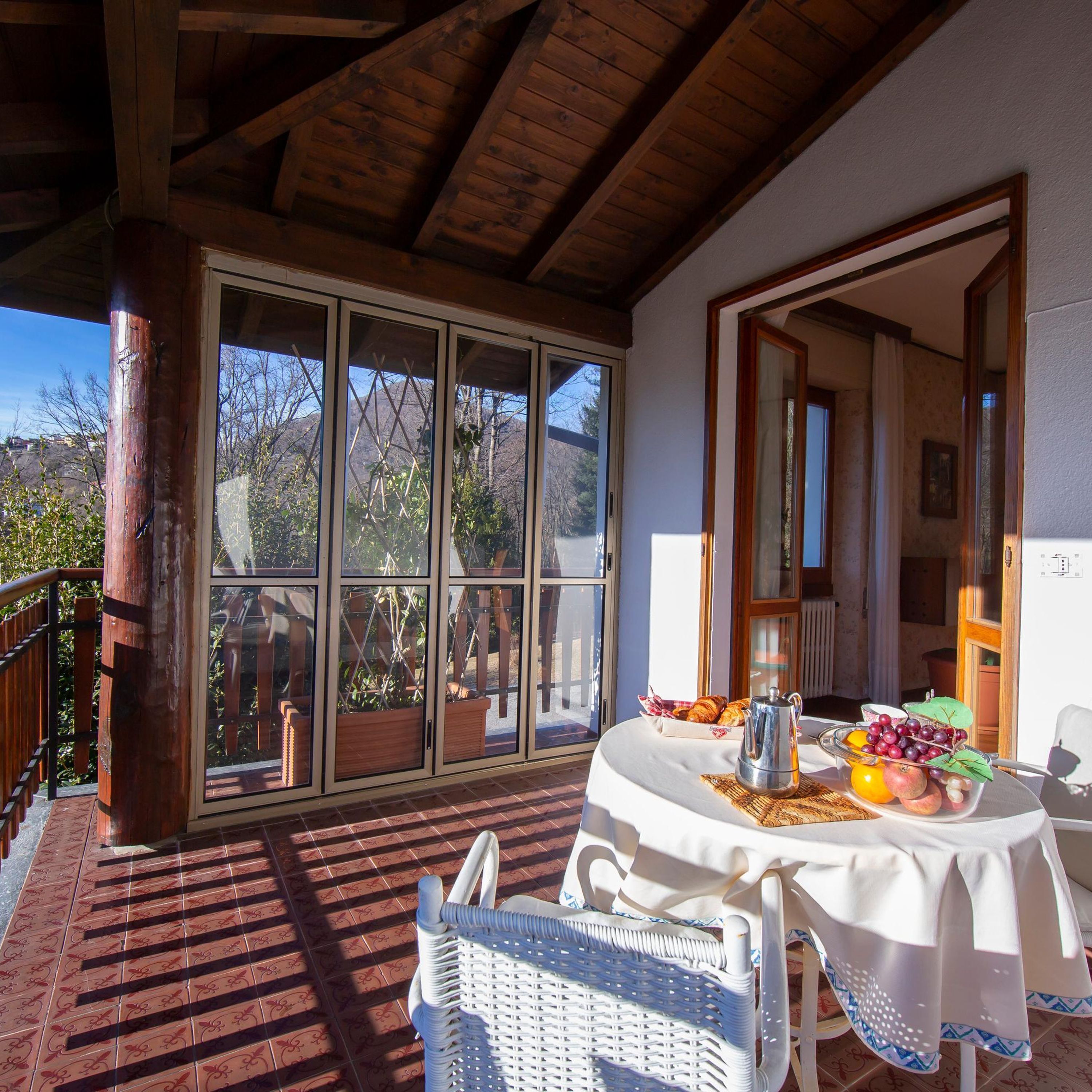 A sunlit patio with a table set for breakfast, a wicker chair, and a view of the outdoors.