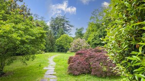 A stone pathway through a lush garden with various trees and shrubs. - Villa La Verbanina Private Garden (Ghiffa)