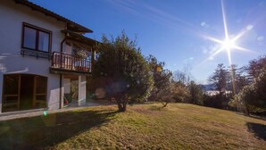 A two-story house with a balcony, a grassy yard, and trees. - Villa La Verbanina Private Garden (Ghiffa)