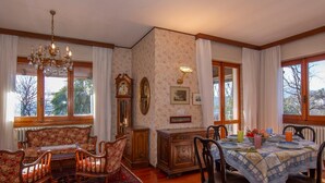 A dining room with a wooden table, chairs, a chandelier, a clock, and a floral wallpaper. - Villa La Verbanina Private Garden (Ghiffa)