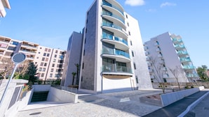 En moderne bygning med flere etager, altaner, en central indgang og en parkeringsplads.
