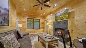 A cozy cabin interior with a wooden ceiling, a fireplace, a sofa, a table, and a chair. - Four Seasons Lodge #4219 (Pigeon Forge)