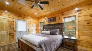 A wooden cabin bedroom with a bed, a nightstand, a ceiling fan, and a window with blinds. - Four Seasons Lodge #4219 (Pigeon Forge)