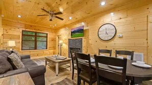 A cozy cabin interior with a wooden ceiling, a fireplace, a dining table with chairs, and a sofa. - Four Seasons Lodge #4219 (Pigeon Forge)
