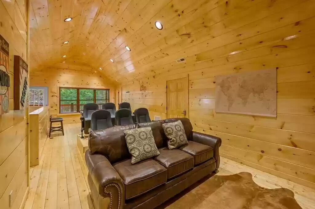 A cozy cabin interior with a wooden ceiling, a leather sofa with patterned cushions, and a map on the wall.