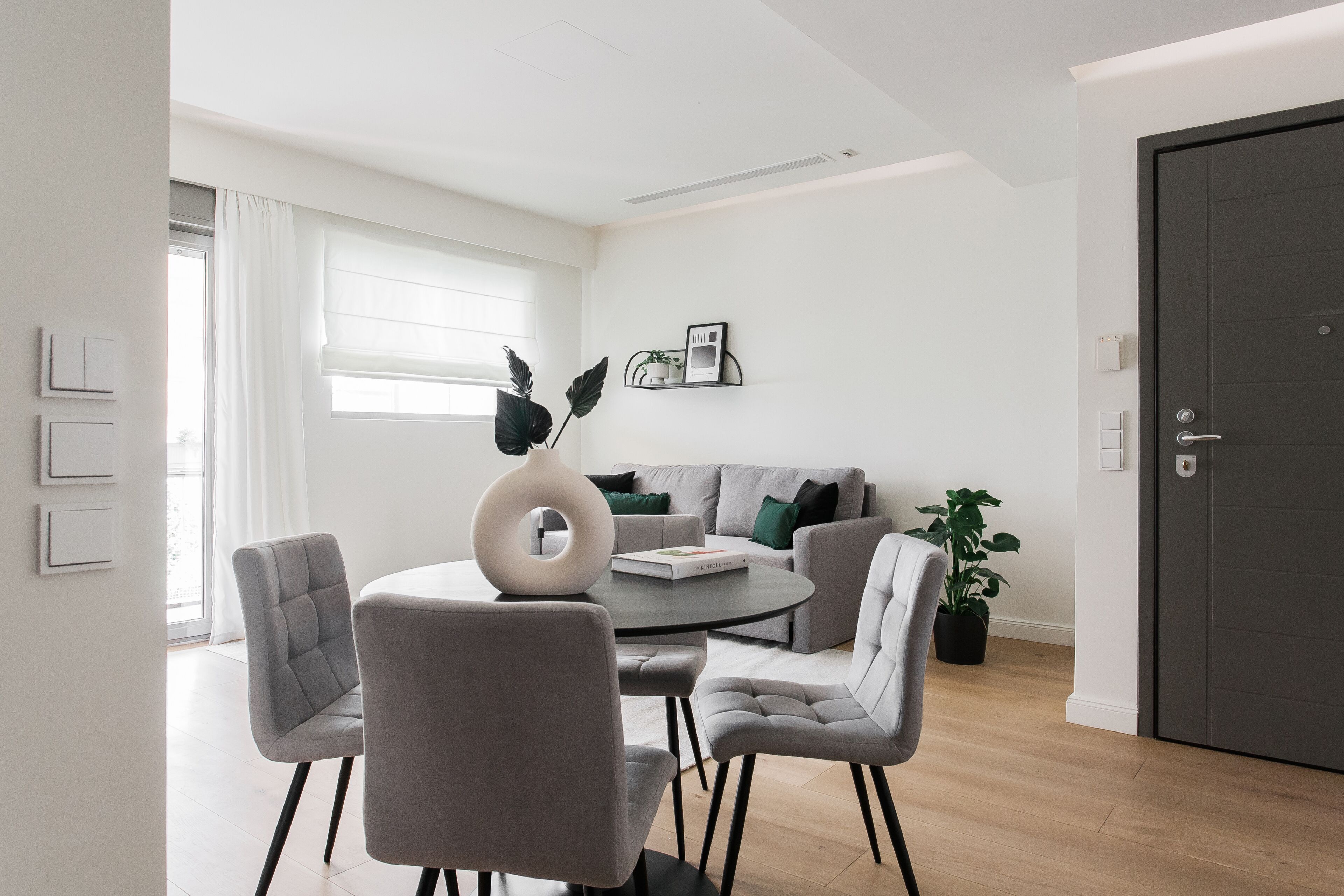 Un salon moderne avec une table ronde, des fauteuils à revêtement gris, un canapé gris et une porte sombre.