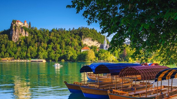 A calm lake with boats docked, a castle on a hill, and lush greenery in the background. - Chalet Kupljenik Near Bled Lake (Bled)