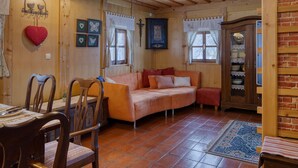 A cozy room with a wooden ceiling, a sofa, a dining table with chairs, and a brick wall. - Chalet Kupljenik Near Bled Lake (Bled)