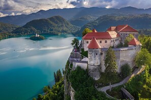 A castle with a tower, surrounded by lush greenery and a lake. - Chalet Kupljenik Near Bled Lake (Bled)