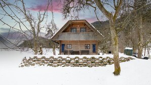 A wooden cabin with a stone wall in front, surrounded by trees and snow. - Chalet Kupljenik Near Bled Lake (Bled)