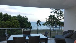 Een balkon met een eettafel en stoelen, een bank en uitzicht op de oceaan en palmbomen.