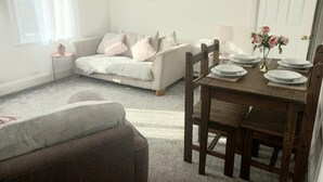 A cozy living room with a white sofa, a wooden dining table set with plates and a vase of flowers, and a painting on the wall. - Clock Tower Flats Morpeth (Morpeth)