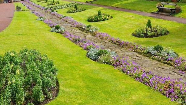 A well-maintained garden with a variety of plants and a pathway leading to a building with a castle-like facade. - Clock Tower Flats Morpeth (Morpeth)