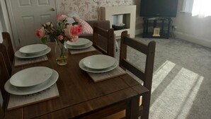 A dining table set with plates, a vase with flowers, and a television in the background. - Clock Tower Flats Morpeth (Morpeth)