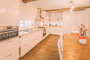 A modern kitchen with white cabinets, a wooden countertop, a stove, and a dining table with chairs. - Douro Mool Guest House (Lamego)