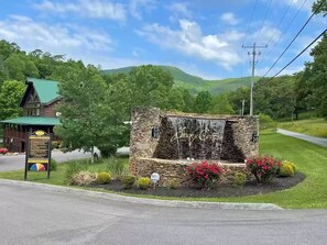 A stone structure with a waterfall feature, surrounded by a landscaped garden with red flowers. - Picture Perfect #439 (Sevierville)