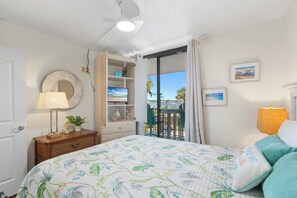 Une chambre à coucher comprenant un lit, une table de chevet, une lampe, un miroir, une étagère avec des objets décoratifs, une fenêtre donnant sur un paysage agréable et un ventilateur de plafond.