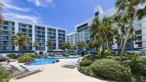 A hotel with a swimming pool surrounded by palm trees and lounge chairs. - Salt and Light Surf & Racquet 204B (Gulf Shores)