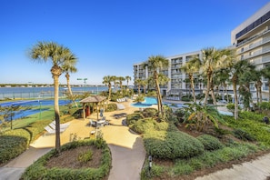 A resort with a pool area, palm trees, and a view of the sea. - Salt and Light Surf & Racquet 204B (Gulf Shores)
