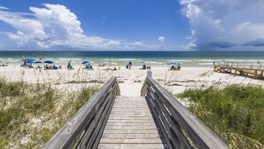A wooden boardwalk leading to a beach with umbrellas and people. - Salt and Light Surf & Racquet 204B (Gulf Shores)