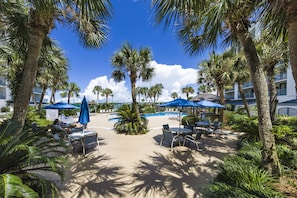 A resort with a pool, palm trees, and outdoor seating areas. - Salt and Light Surf & Racquet 204B (Gulf Shores)