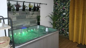 Une pièce dotée d’un jacuzzi, d’un mur en bois orné de plantes suspendues et d’un papier peint aux motifs tropicaux sur le mur adjacent.