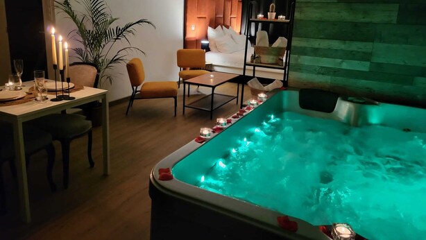 Une chambre moderne dotée d’un jacuzzi, d’un coin repas éclairé à la bougie et d’un espace salon confortable.
