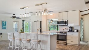 Une cuisine moderne dotée d’un îlot central, de tabourets de bar, d’appareils électroménagers en acier inoxydable et de luminaires suspendus.