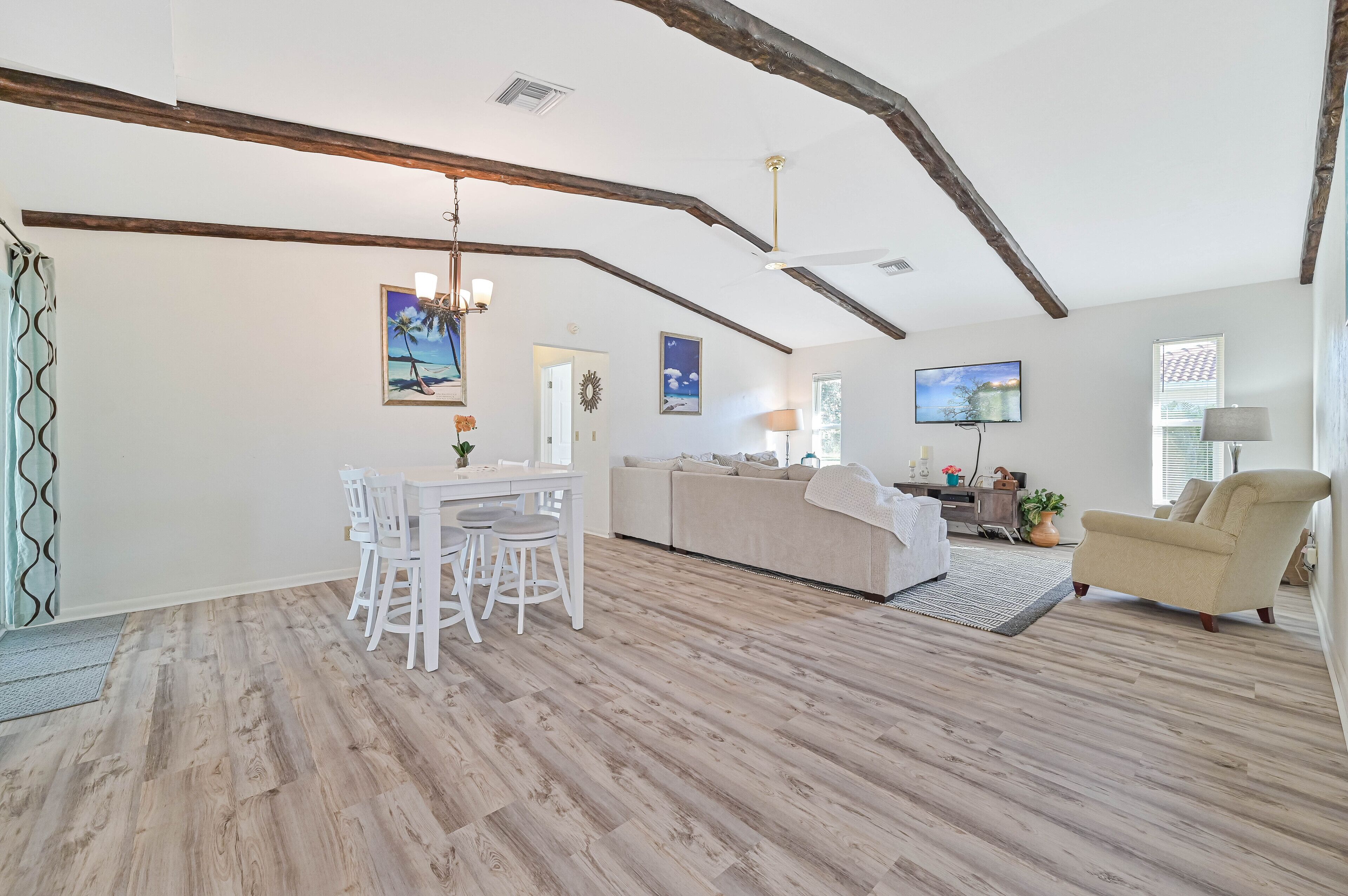 Una sala de estar amplia con suelo de madera, un sofá blanco, un sillón color beige y un comedor con mesa y sillas blancas.