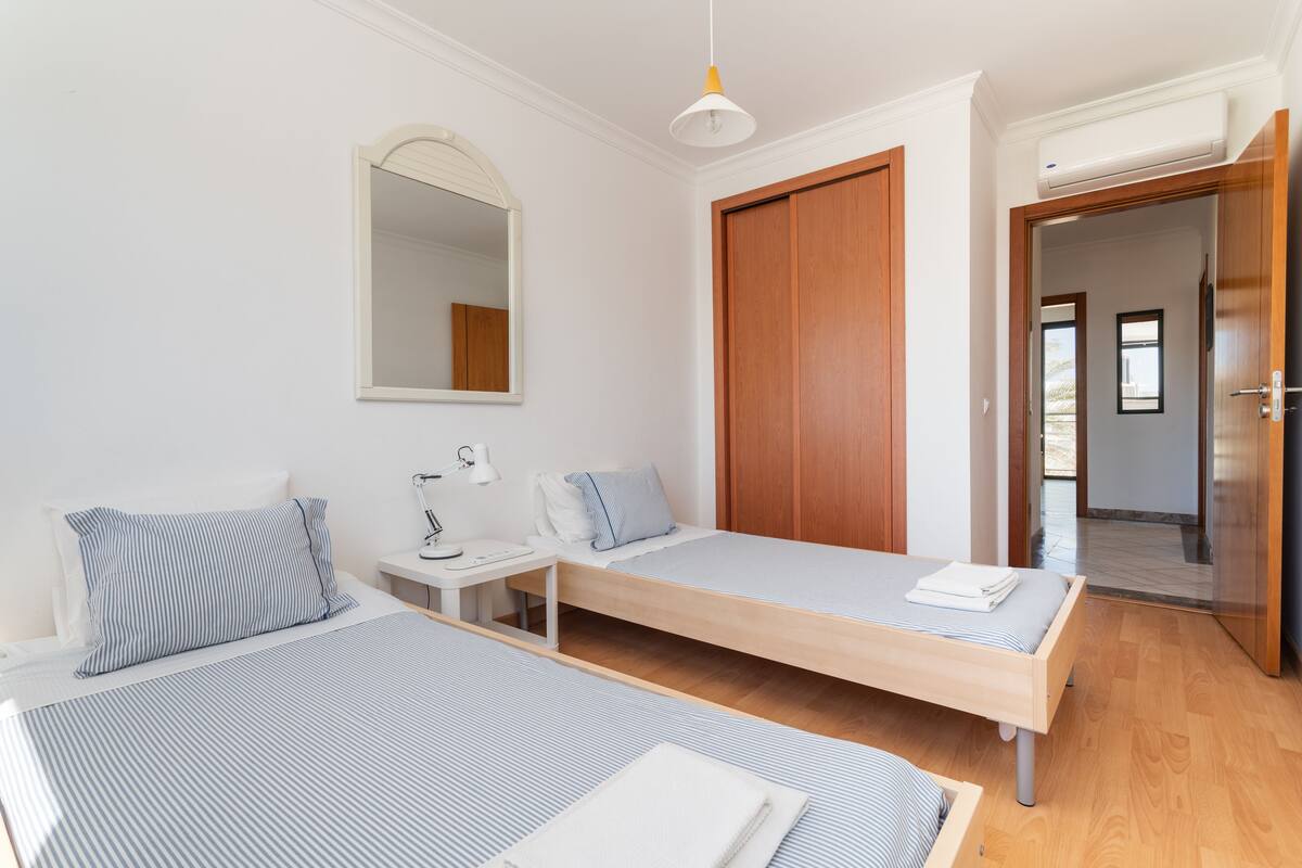 Une chambre moderne avec deux lits simples, une table de chevet avec une lampe, un miroir et une armoire.