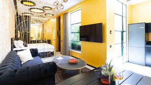 A modern living room with a sofa, a round coffee table, and a TV mounted on the wall. - The Shell House (Tel Aviv)