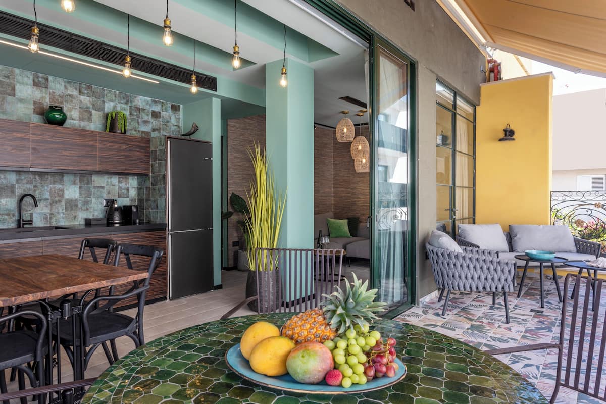 A modern kitchen with a dining area, a fruit bowl on the table, and a patio with seating.