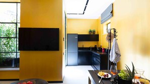 A modern kitchen with a flat-screen TV, a dining table with fruit and a drink, and a view of the outdoors. - The Shell House (Tel Aviv)