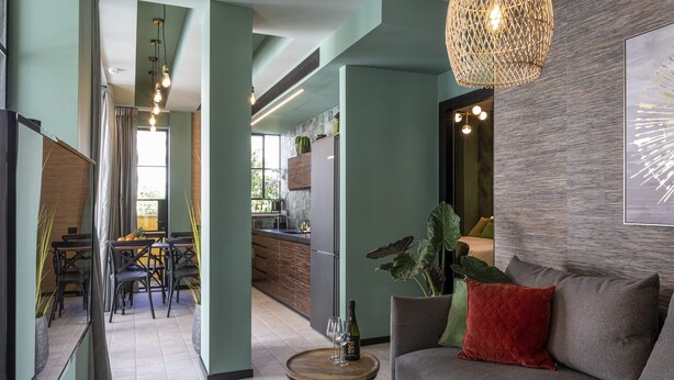 A modern living room with a grey sofa, a small wooden coffee table, and a red cushion. A dining area with a table and chairs is visible in the background. - The Shell House (Tel Aviv)