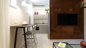 A modern kitchen with a dining area, a wooden accent wall, and a TV mounted on the wall. - The Shell House (Tel Aviv)