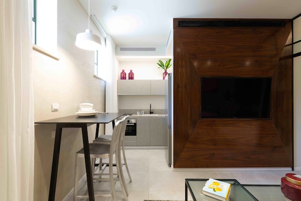 A modern kitchen with a dining area, a wooden accent wall, and a TV mounted on the wall. - The Shell House (Tel Aviv)