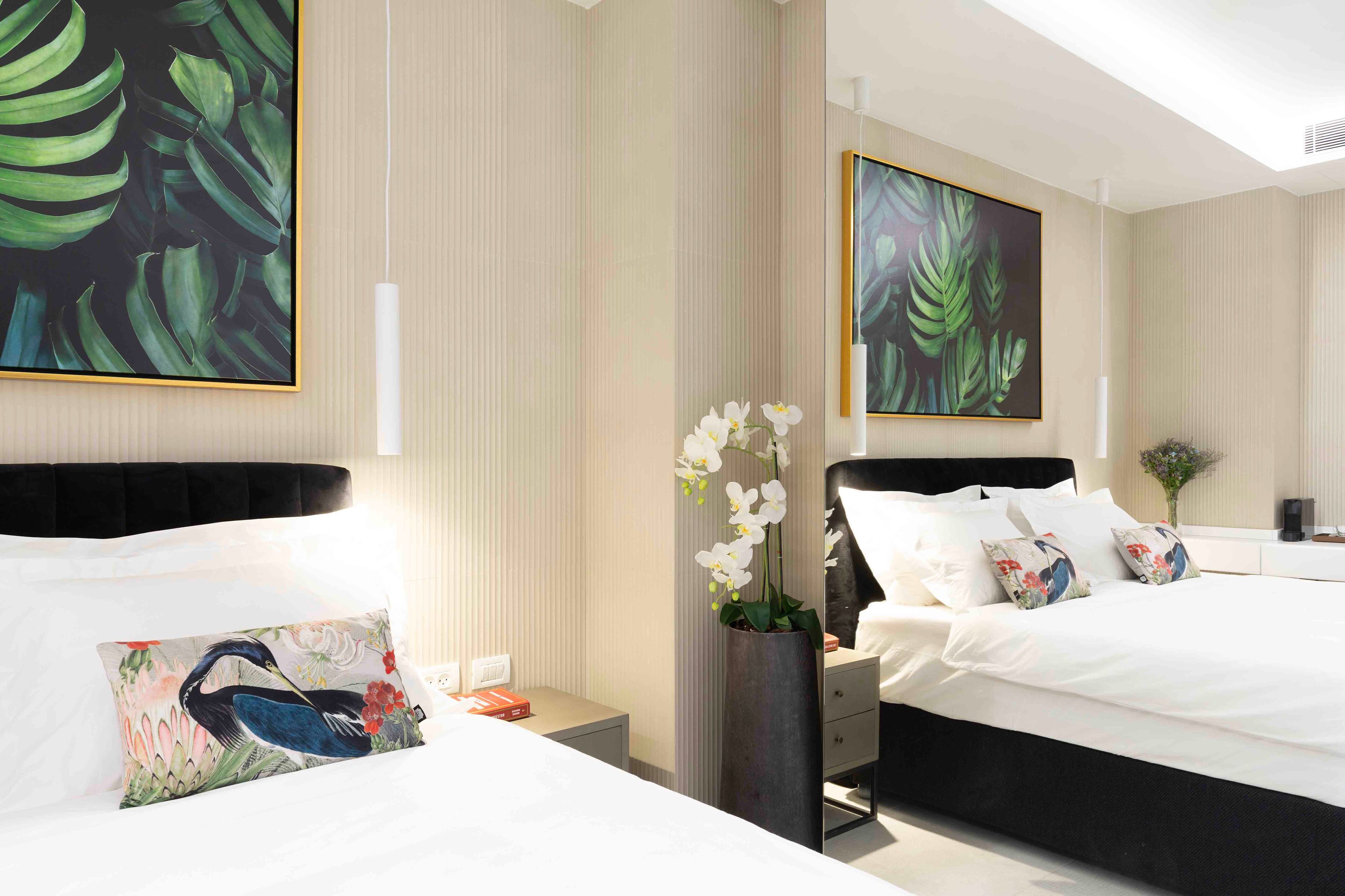 Habitación de hotel con dos camas, una mesita de noche, un jarrón con flores blancas y obras de arte en las paredes.