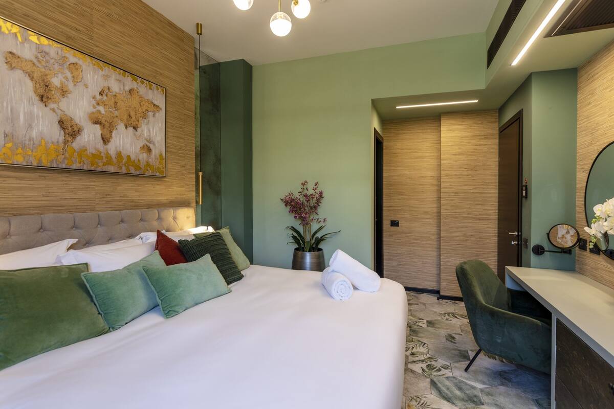 A modern hotel room with a large bed, a desk, and a potted plant.